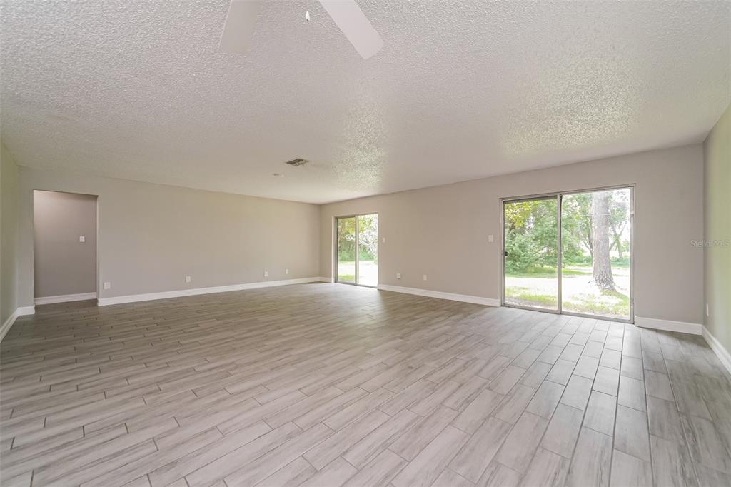 An empty living room features light gray wood-look tile flooring and two sliding glass doors — 10346 MATCHLOCK DRIVE, ORLANDO, FL