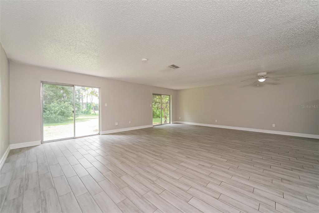 A spacious, empty room features light gray wood-look tile flooring and two sliding glass doors — 10346 MATCHLOCK DRIVE, ORLANDO, FL