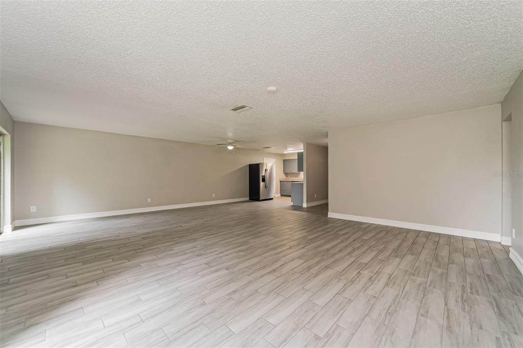 A spacious, open-concept living area features light-colored wood-look tile flooring and neutral wall paint — 10346 MATCHLOCK DRIVE, ORLANDO, FL
