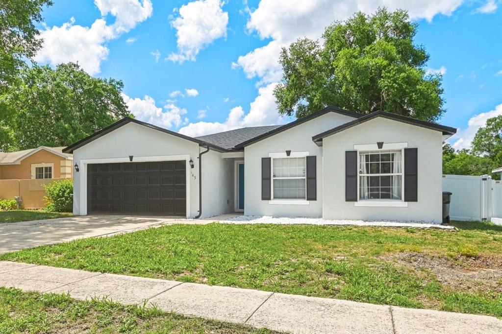 A single-story house with a white stucco exterior, black shutters, and a two-car garage — 143 LAUREL RIDGE AVENUE, OCOEE, FL