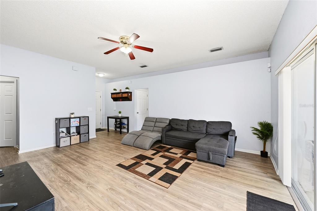 A living room features light-colored wood flooring, a gray sectional sofa, and a ceiling fan — 143 LAUREL RIDGE AVENUE, OCOEE, FL