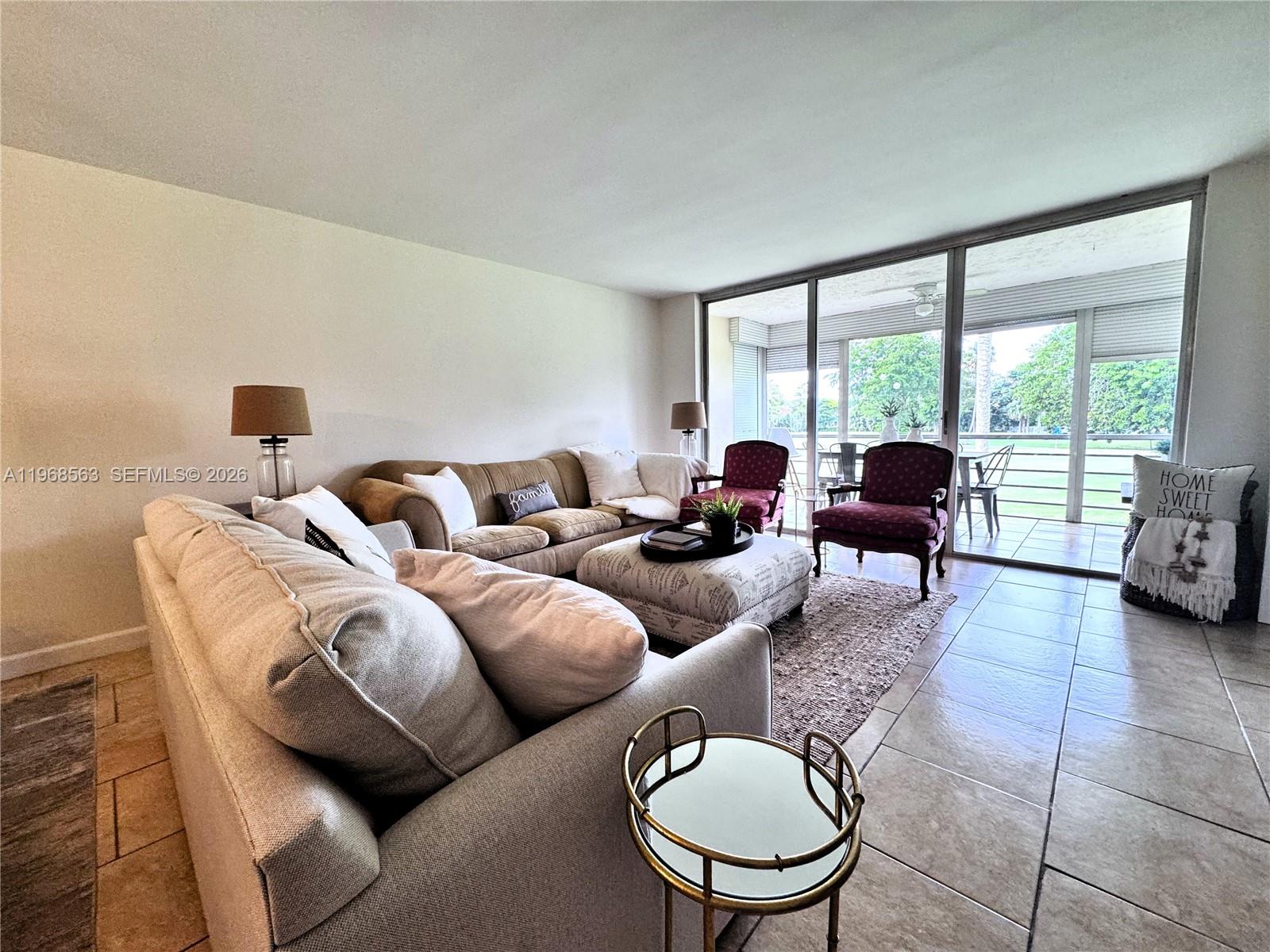 A living room features a beige sofa, patterned ottoman, two armchairs, and sliding glass doors — 901 W Cypress Ln # 201, Pompano Beach FL 33069, POMPANO BEACH, FL