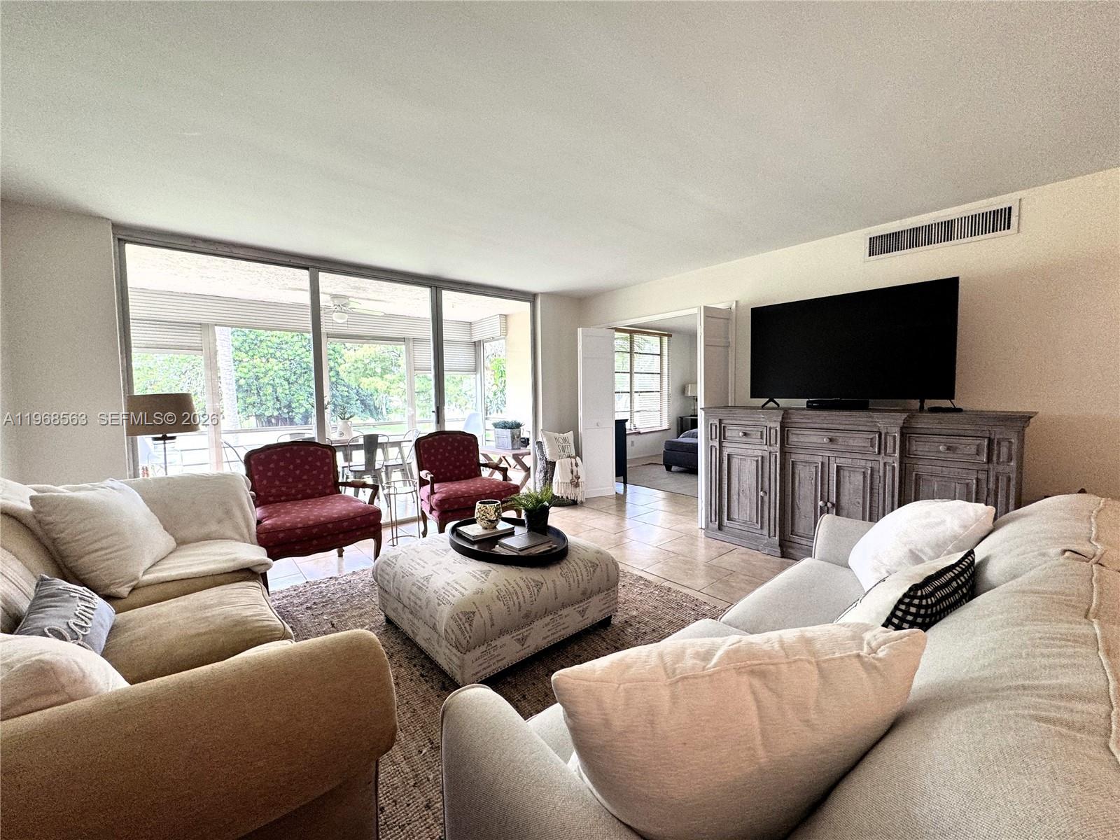A living room features a large television on a wooden console, sofas, and sliding glass doors — 901 W Cypress Ln # 201, Pompano Beach FL 33069, POMPANO BEACH, FL