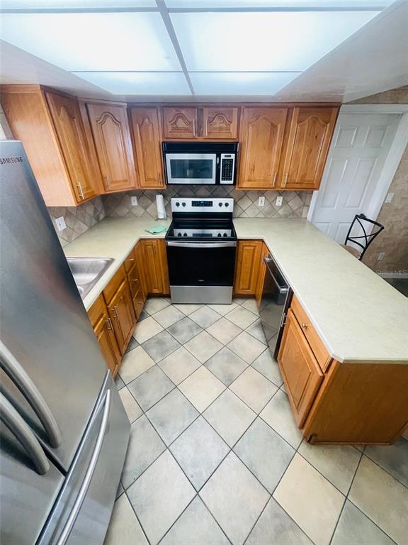 A kitchen features wood cabinets, stainless steel appliances, and light-colored countertops over tile flooring — 999 ELEANOR AVENUE, DELTONA, FL