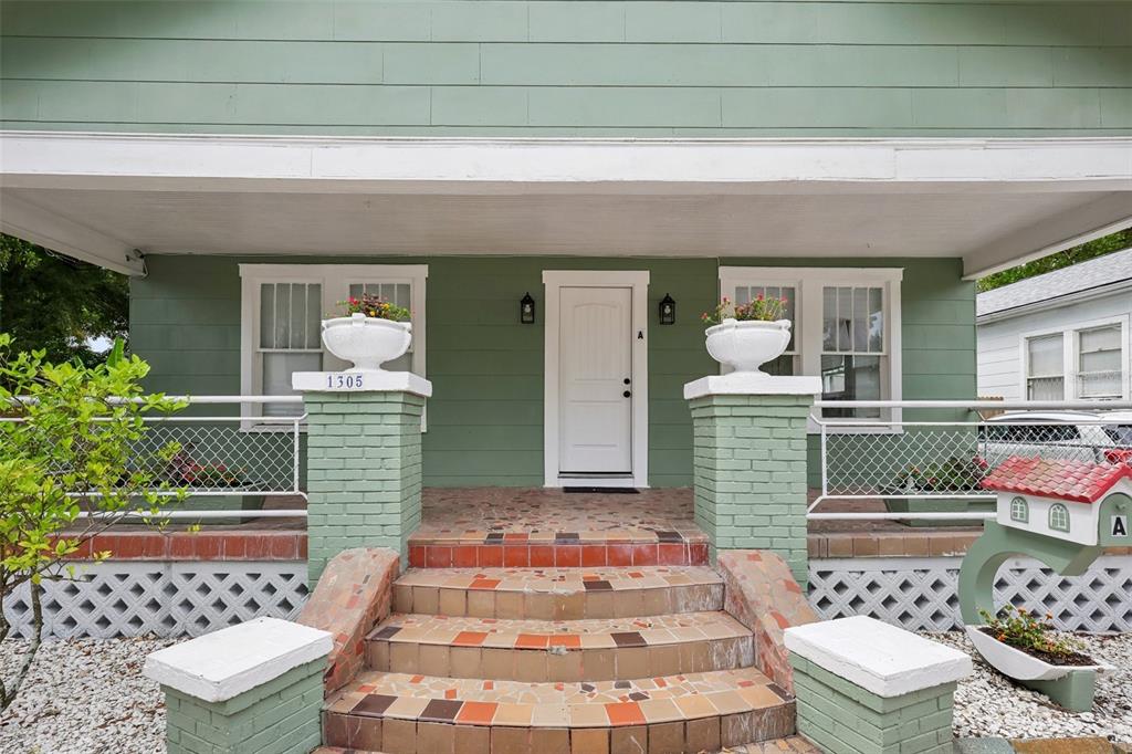 A green house exterior features a tiled front porch with brick pillars and white railings — 1305 E 17TH AVENUE, TAMPA, FL