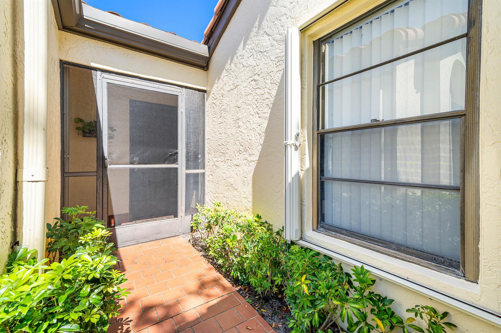 A brick walkway leads to a screened front door beside a window with vertical blinds — 10069 Andrea Lane # A, Boynton Beach FL 33437, BOYNTON BEACH, FL