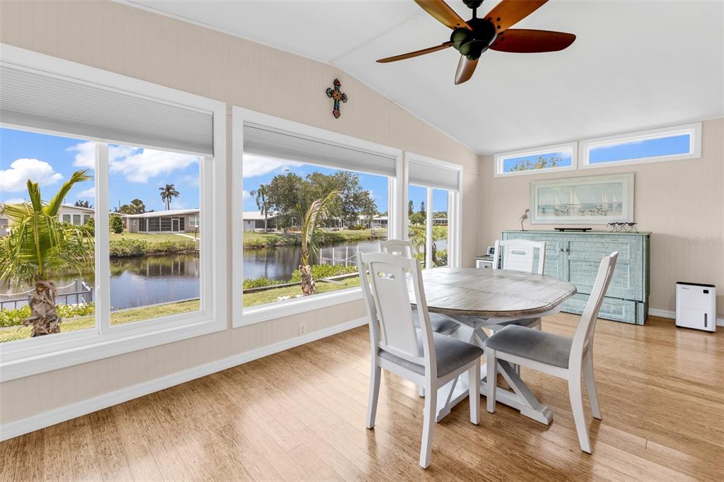 A dining room with a round table, white chairs, wood flooring, and large windows overlooking water — 114 MARTINIQUE ROAD, NORTH PORT, FL