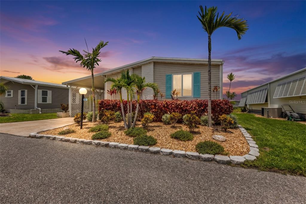 A single-story manufactured home with light siding, turquoise shutters, and a landscaped front yard — 114 MARTINIQUE ROAD, NORTH PORT, FL