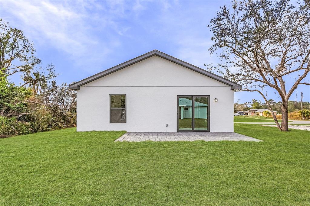 The back exterior of a white house features a paved patio, a window, and sliding doors — 2817 SNUG STREET, NORTH PORT, FL