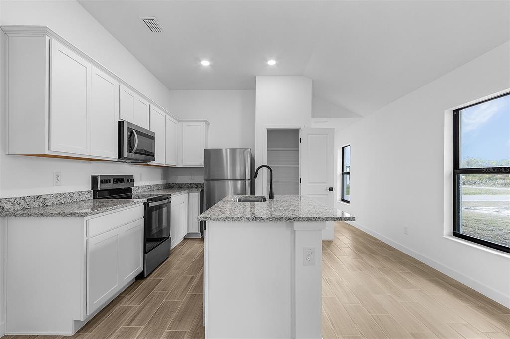 A modern kitchen features white cabinets, granite countertops, stainless steel appliances, and light wood flooring — 2817 SNUG STREET, NORTH PORT, FL