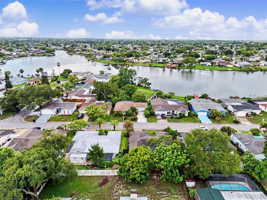 An aerial view shows a residential neighborhood with houses situated along a lakefront — 9641 LAKESIDE LANE, PORT RICHEY, FL