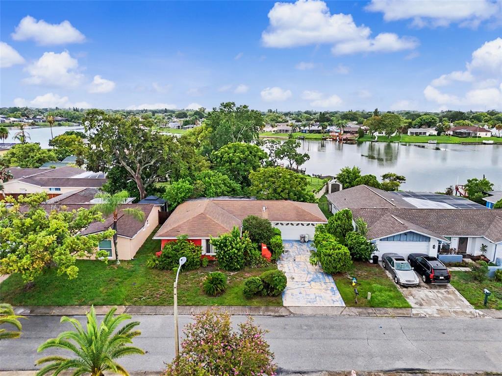 An aerial view shows a red house with a brown roof situated near a lake — 9641 LAKESIDE LANE, PORT RICHEY, FL