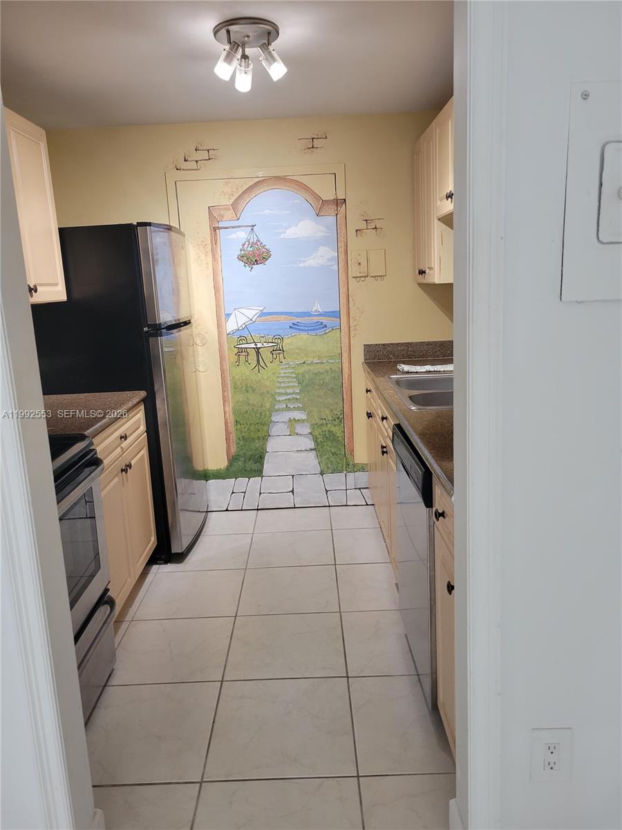 A galley kitchen features light-colored cabinets, stainless steel appliances, and a mural on the back wall — 2020 NE 135th St # 904, North Miami FL 33181, NORTH MIAMI, FL