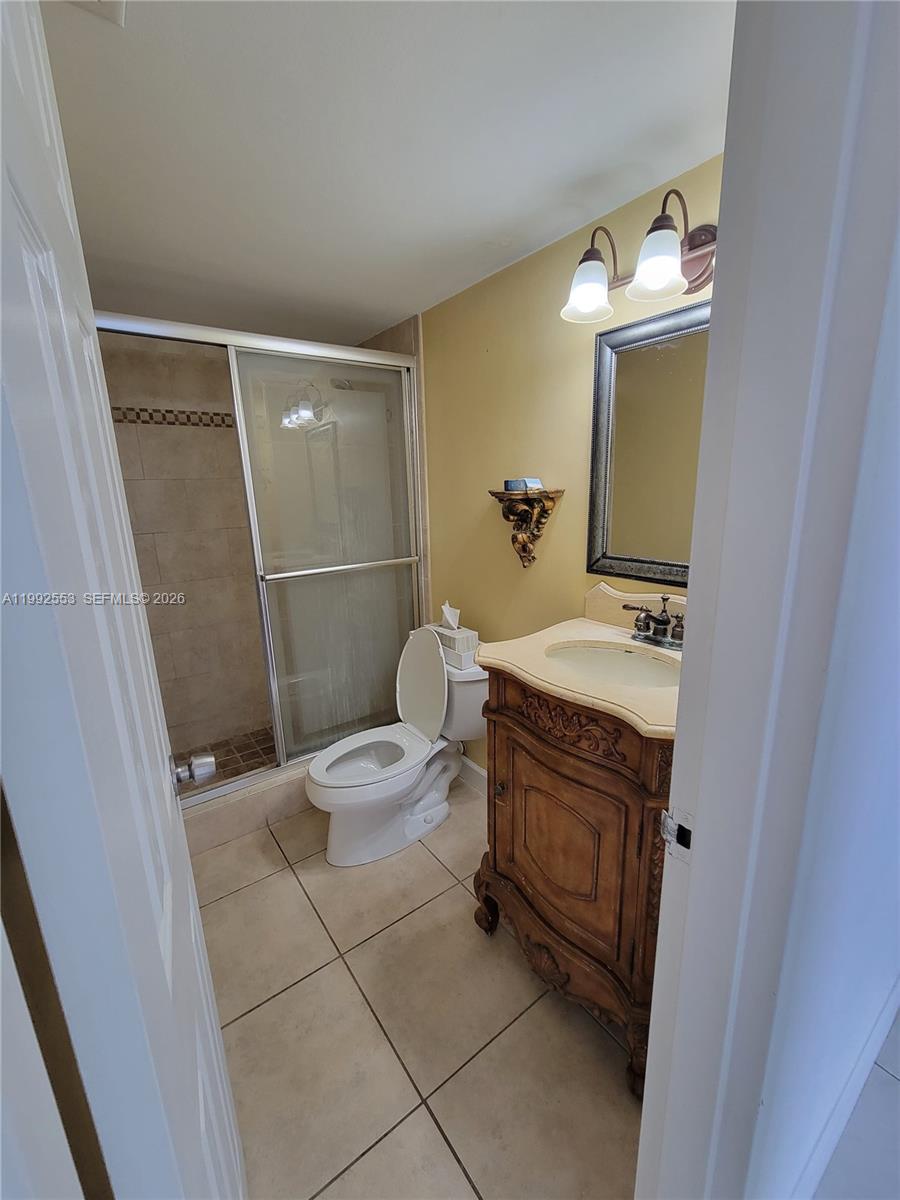 A bathroom features a walk-in shower, a pedestal vanity, and a toilet on tiled flooring — 2020 NE 135th St # 904, North Miami FL 33181, NORTH MIAMI, FL