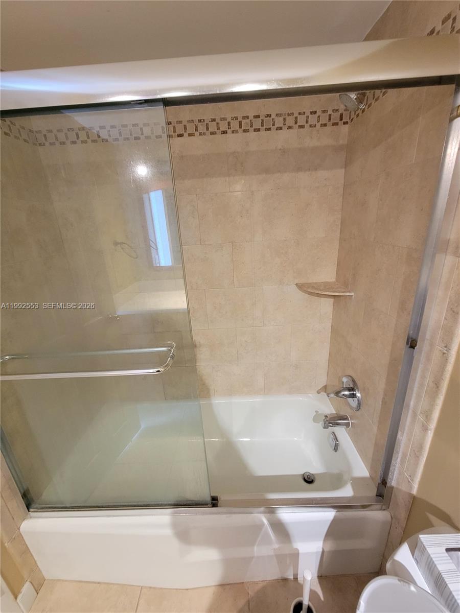 A bathroom features a white bathtub with a glass sliding door and beige tiled walls — 2020 NE 135th St # 904, North Miami FL 33181, NORTH MIAMI, FL