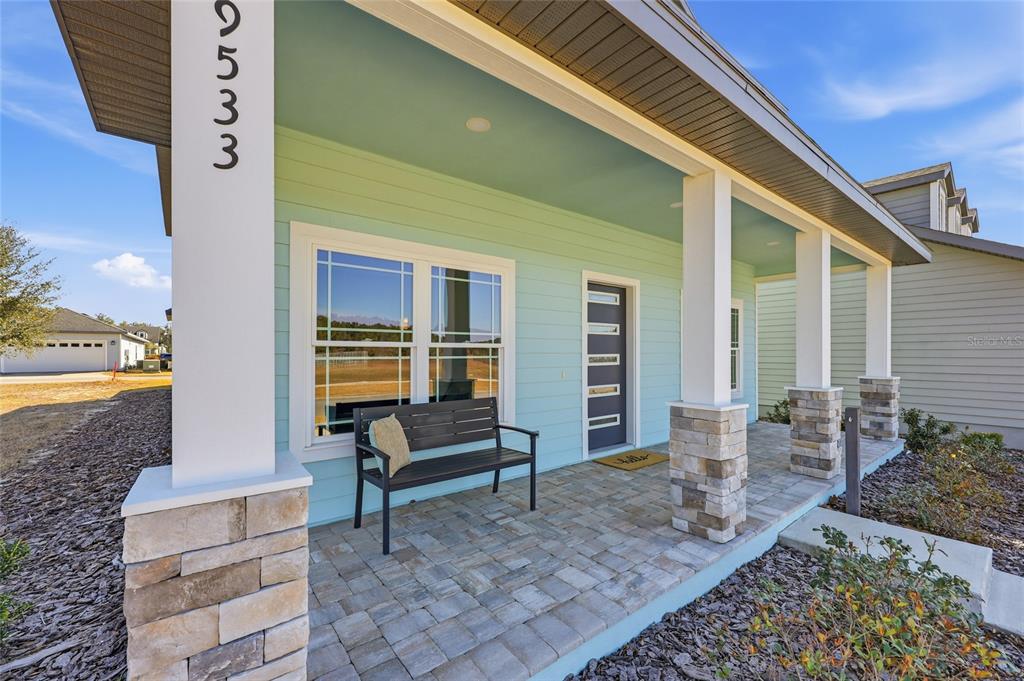 A light blue house exterior features a stone-based porch with a bench and front door — 9533 SW 66TH LANE, GAINESVILLE, FL