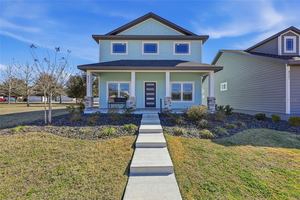 A light blue two-story house features a front porch, stone columns, and a concrete walkway — 9533 SW 66TH LANE, GAINESVILLE, FL