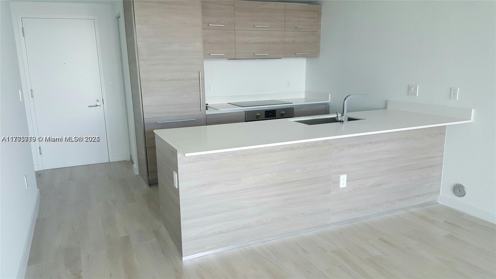 A modern kitchen features light wood cabinetry, white countertops, and a central island — 1300 S Miami Ave # 4411, Miami FL 33130, MIAMI, FL