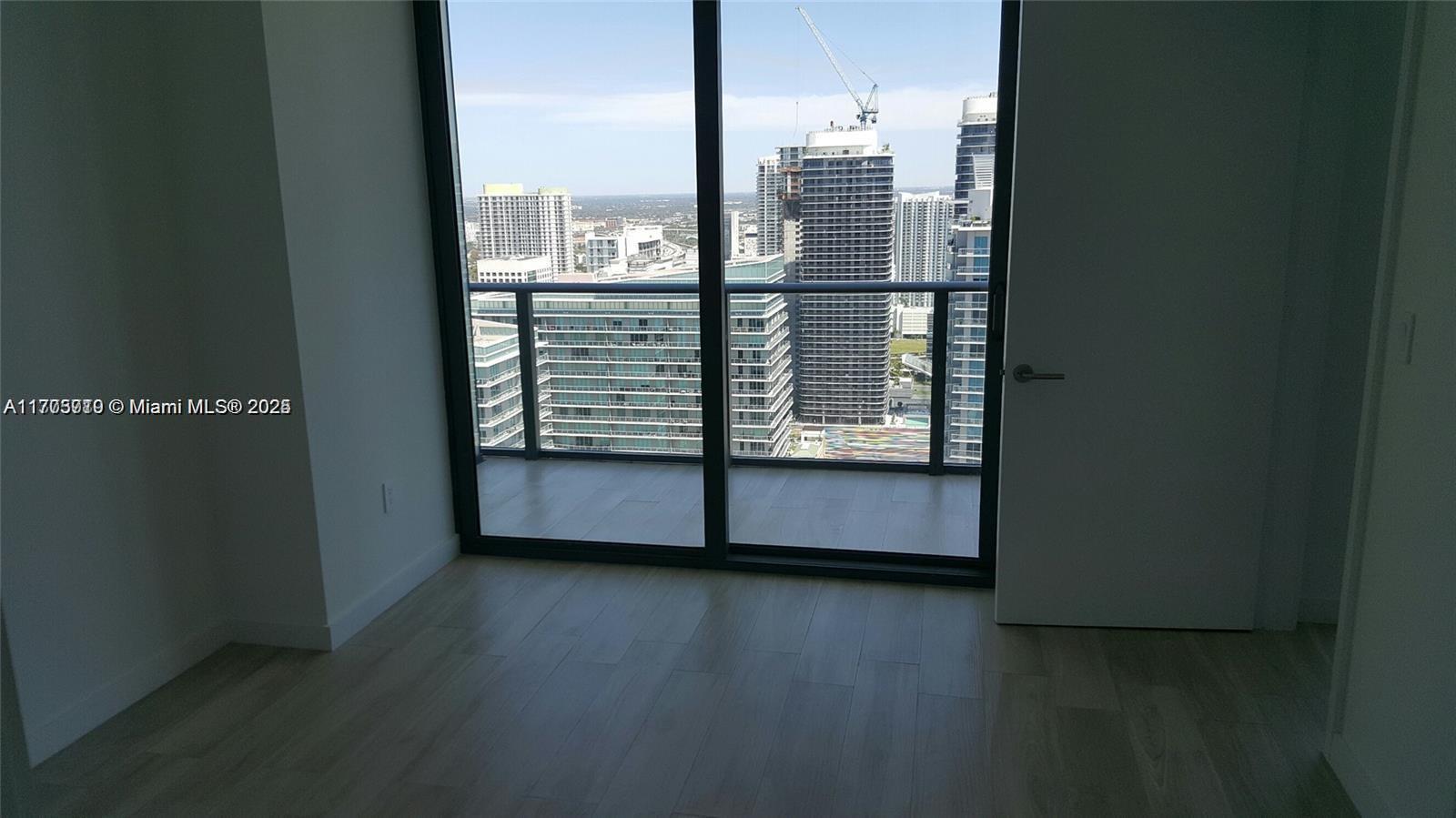 An interior room with light wood flooring features a sliding glass door leading to a balcony — 1300 S Miami Ave # 4411, Miami FL 33130, MIAMI, FL