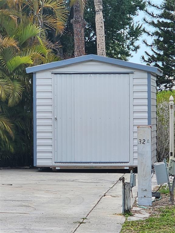 A light-colored metal storage shed sits on a concrete pad near a utility post — 1674 UNIVERSITY PARKWAY UNIT 328, SARASOTA, FL