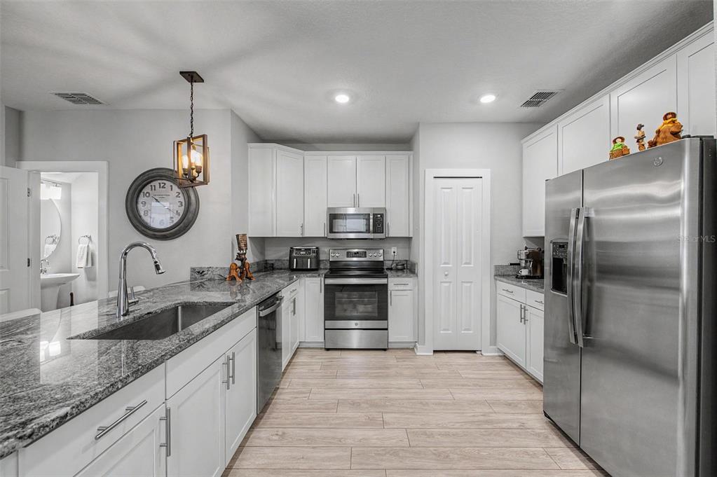 A kitchen features white cabinets, granite countertops, stainless steel appliances, and light wood-look flooring — 6023 INTERBAY BOULEVARD UNIT 1, TAMPA, FL