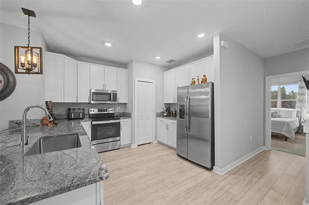 A kitchen with white cabinets, stainless steel appliances, and granite countertops features light wood flooring — 6023 INTERBAY BOULEVARD UNIT 1, TAMPA, FL