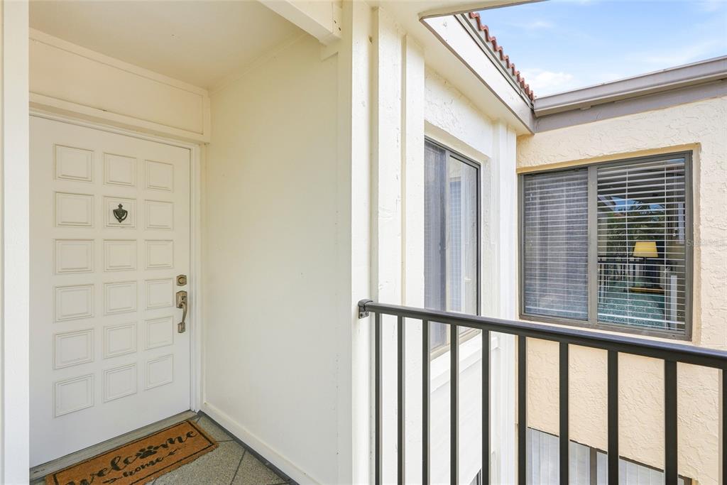 A white front door with a welcome mat sits on a balcony with black railings — 6105 PALMA DEL MAR BOULEVARD S UNIT 219, ST PETERSBURG, FL