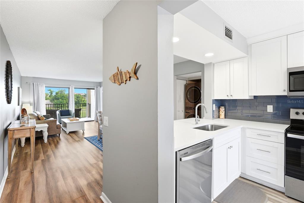 A kitchen with white cabinets and a stainless steel dishwasher overlooks a living area — 6105 PALMA DEL MAR BOULEVARD S UNIT 219, ST PETERSBURG, FL