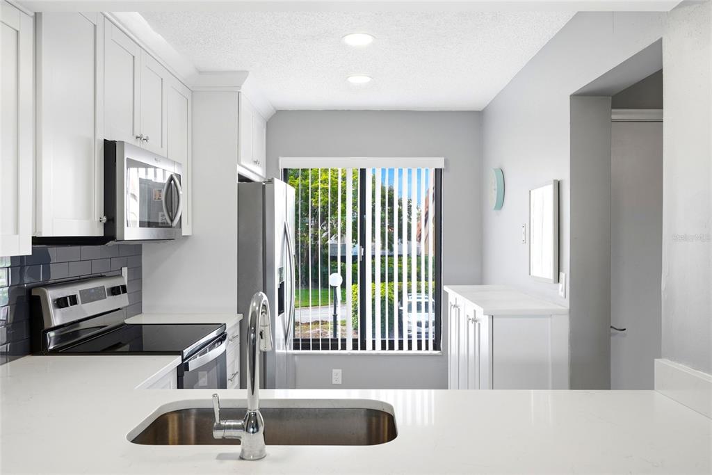 A kitchen with white cabinets, stainless steel appliances, a sink, and a window with blinds — 6105 PALMA DEL MAR BOULEVARD S UNIT 219, ST PETERSBURG, FL