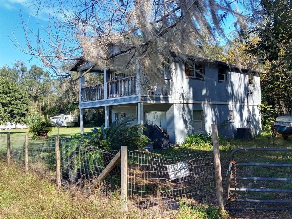 A two-story house with a wooden balcony and metal siding stands behind a wire fence — 9895 NE 30TH COURT, ANTHONY, FL