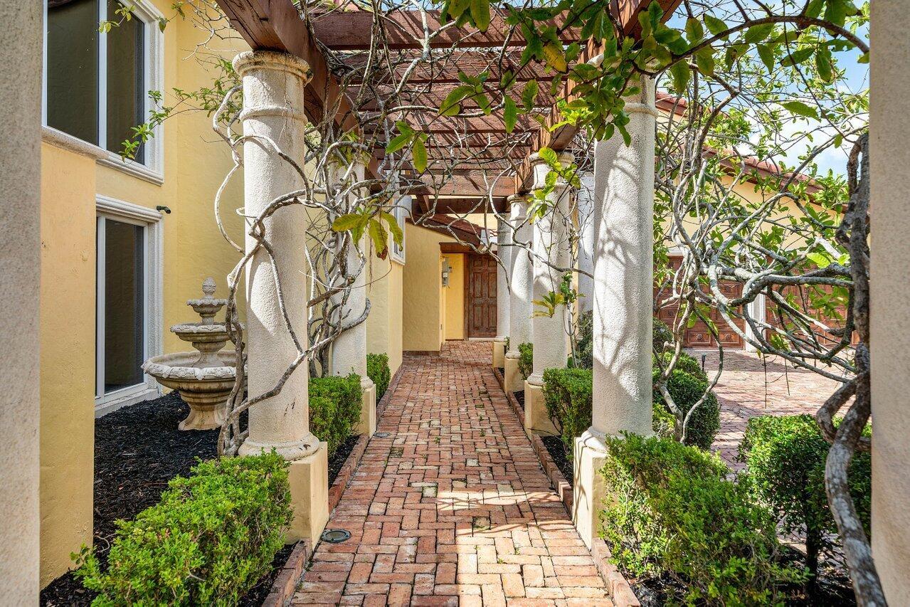 A brick walkway leads to a wooden door under a pergola supported by stone columns — 6541 Timber Lane, Boca Raton FL 33433, BOCA RATON, FL
