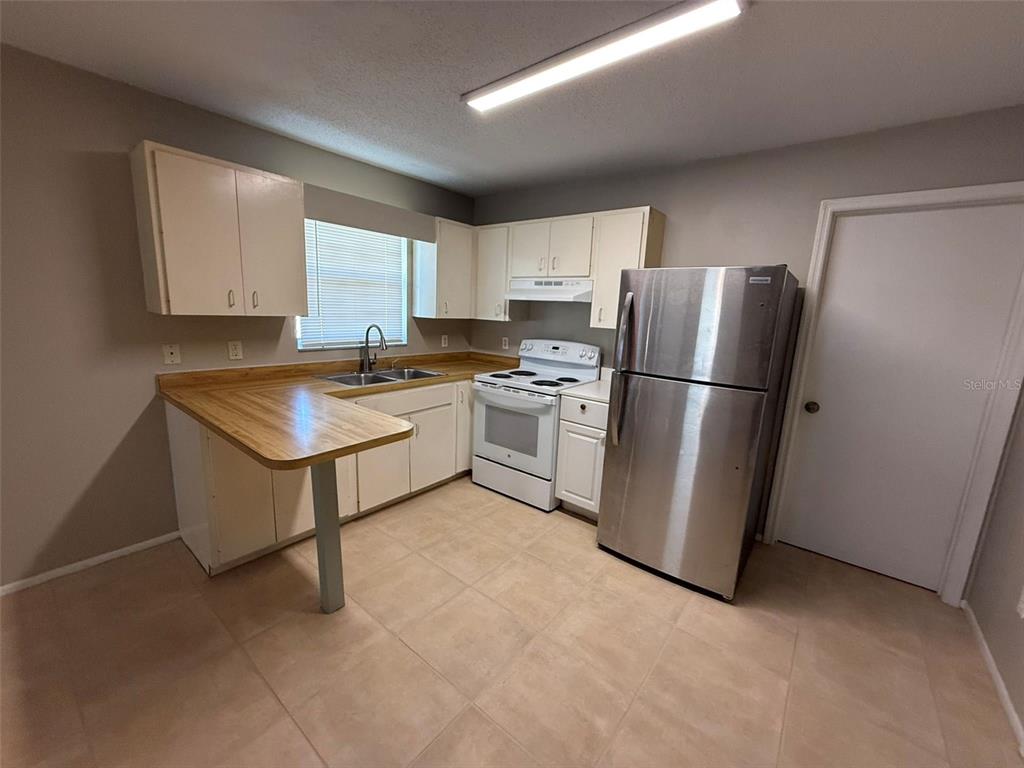 A kitchen features light-colored cabinets, a wood-look countertop, white appliances, and a stainless steel refrigerator — 11081 PENDLETON AVENUE UNIT A, ENGLEWOOD, FL