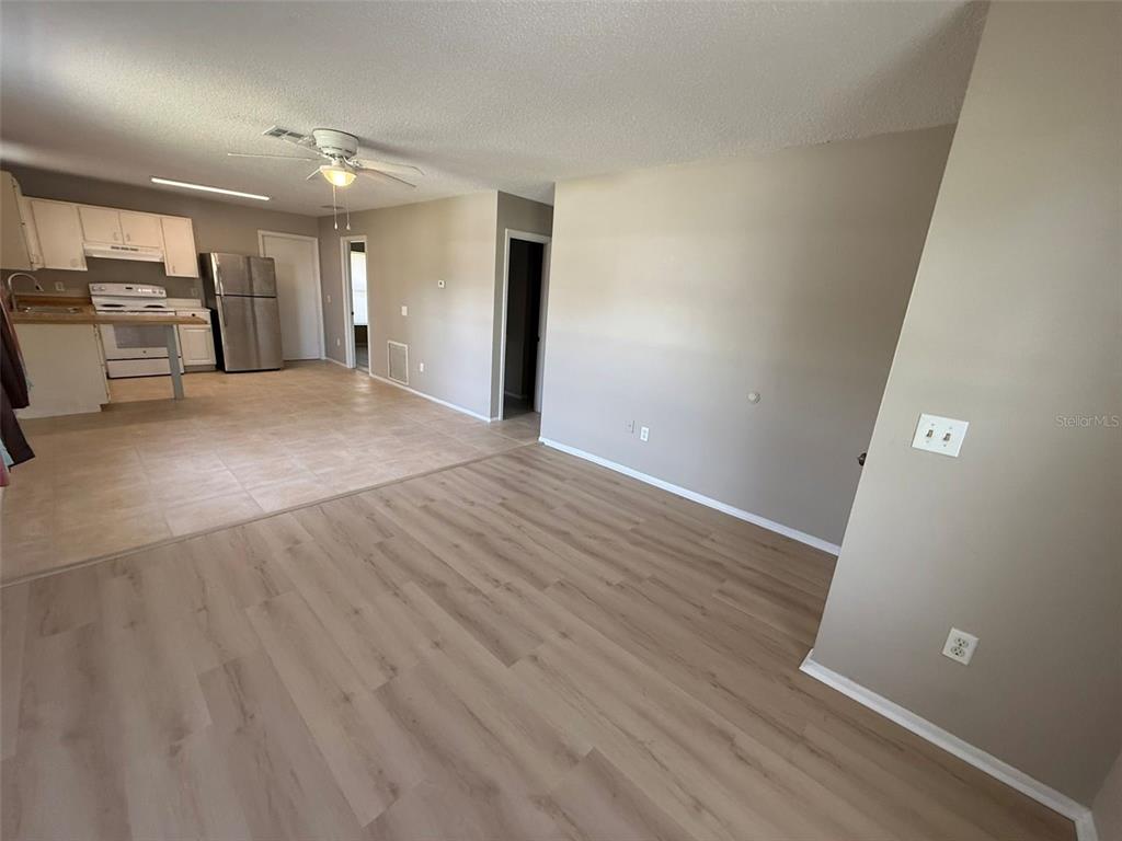 An open-concept living area with light wood-look flooring transitions into a tiled kitchen — 11081 PENDLETON AVENUE UNIT A, ENGLEWOOD, FL
