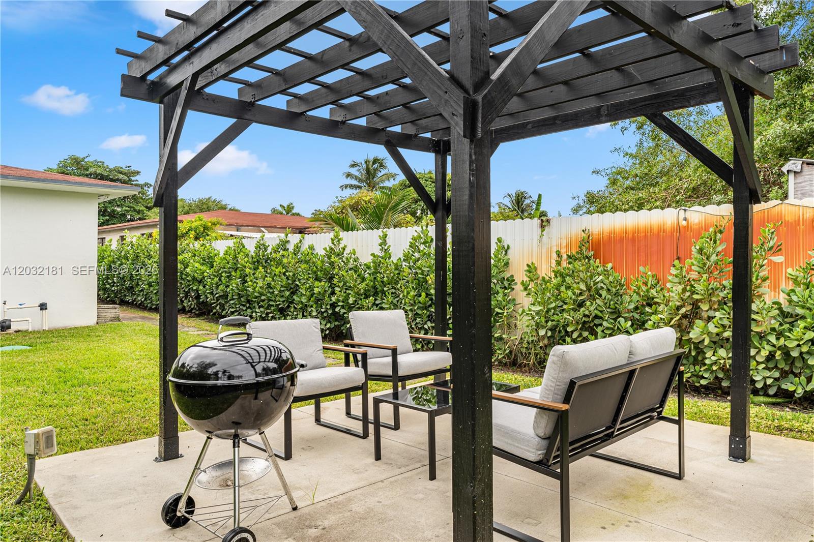 A black wooden pergola stands over a patio with outdoor furniture and a charcoal grill — 1521 NE 118th Ter # 1, Miami FL 33161, MIAMI, FL