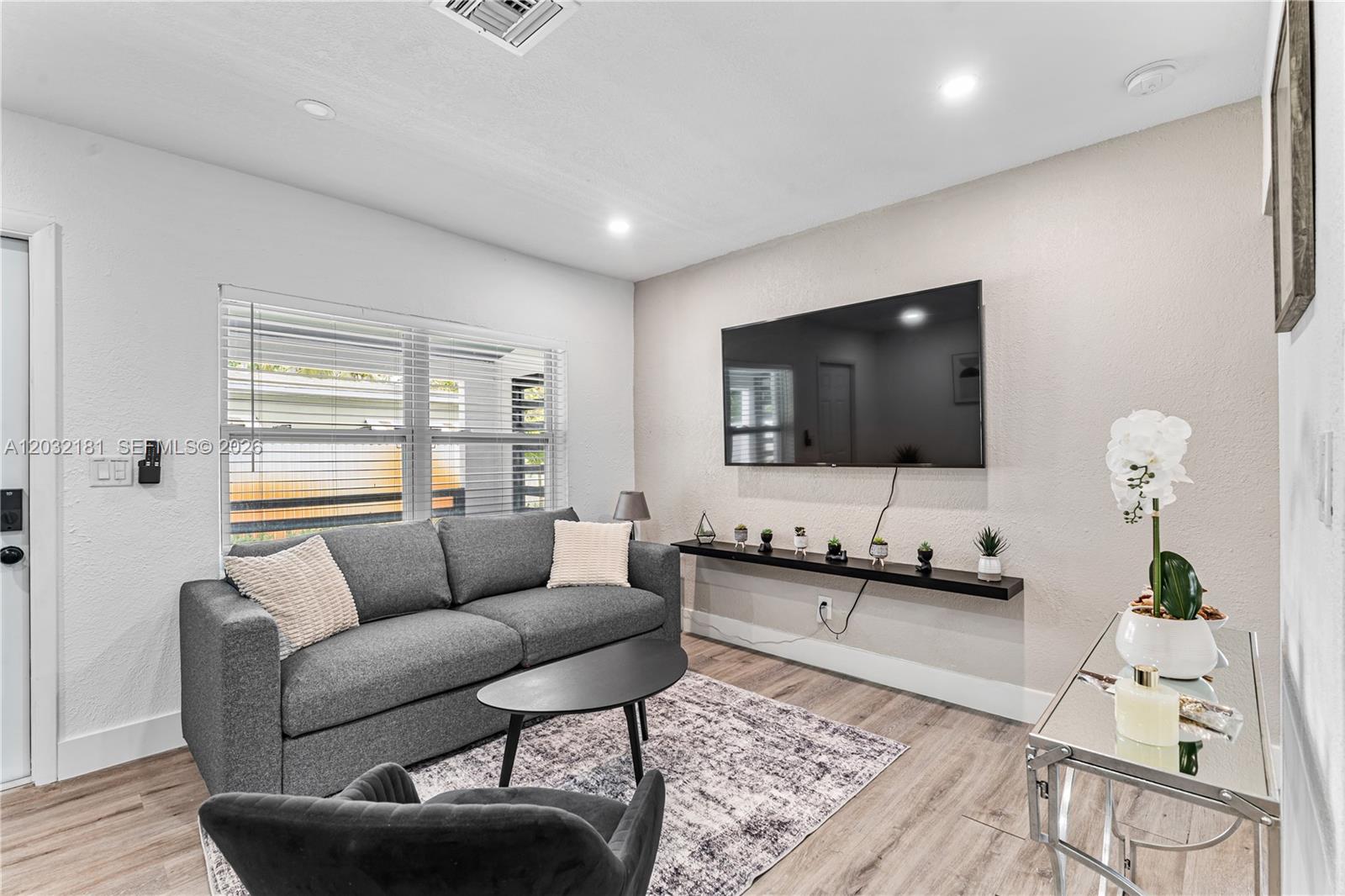 A living room features a grey sofa, a wall-mounted television, and a floating shelf — 1521 NE 118th Ter # 1, Miami FL 33161, MIAMI, FL