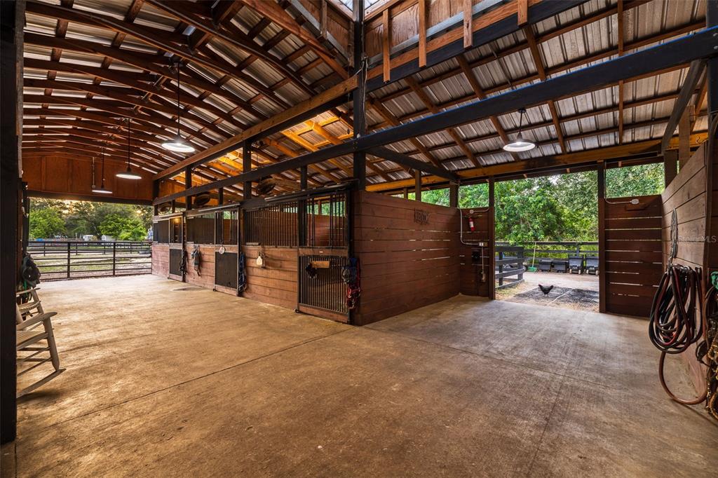 An open-air horse stable features concrete flooring, wooden stalls with metal grates, and exposed rafters — 8701 64TH STREET N, PINELLAS PARK, FL
