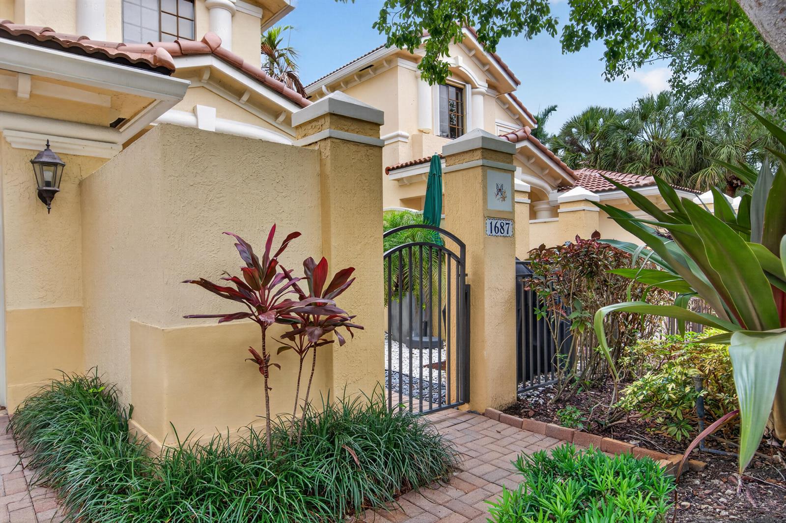 A yellow stucco house exterior features a gated courtyard entrance with a brick walkway — 1687 Passion Vine Circle # 1687, Weston FL 33326, WESTON, FL