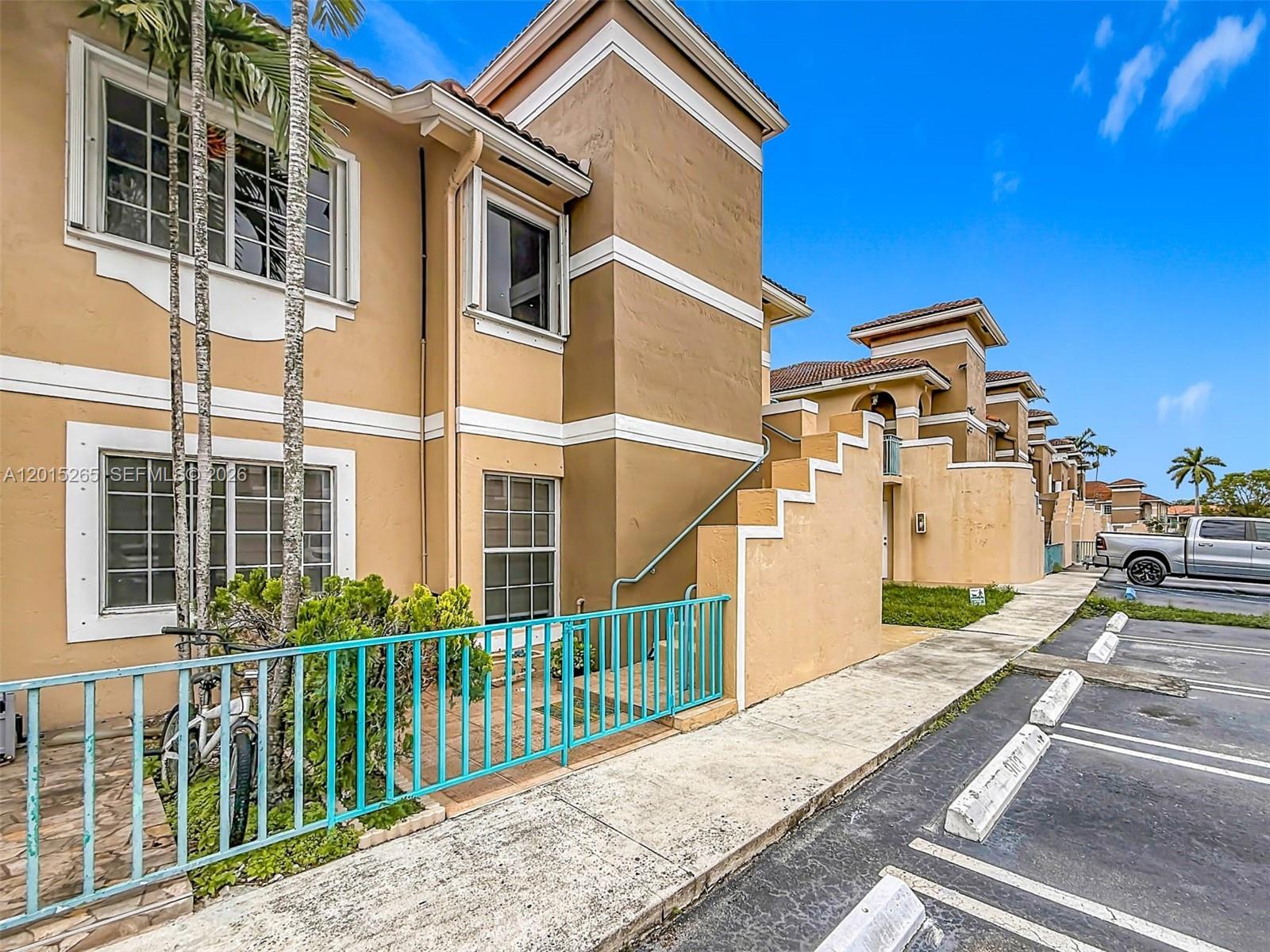 An exterior view of a multi-story tan apartment building with a turquoise metal fence — 6466 SW 130th Pl # 902, Miami FL 33183, MIAMI, FL