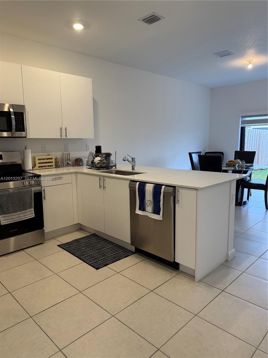 A modern kitchen features white cabinets, stainless steel appliances, and a quartz-topped peninsula — 12955 SW 231st Ter # 12955, Miami FL 33170, MIAMI, FL