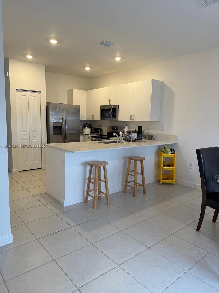 A kitchen features white cabinets, stainless steel appliances, a breakfast bar, and tile flooring — 12955 SW 231st Ter # 12955, Miami FL 33170, MIAMI, FL