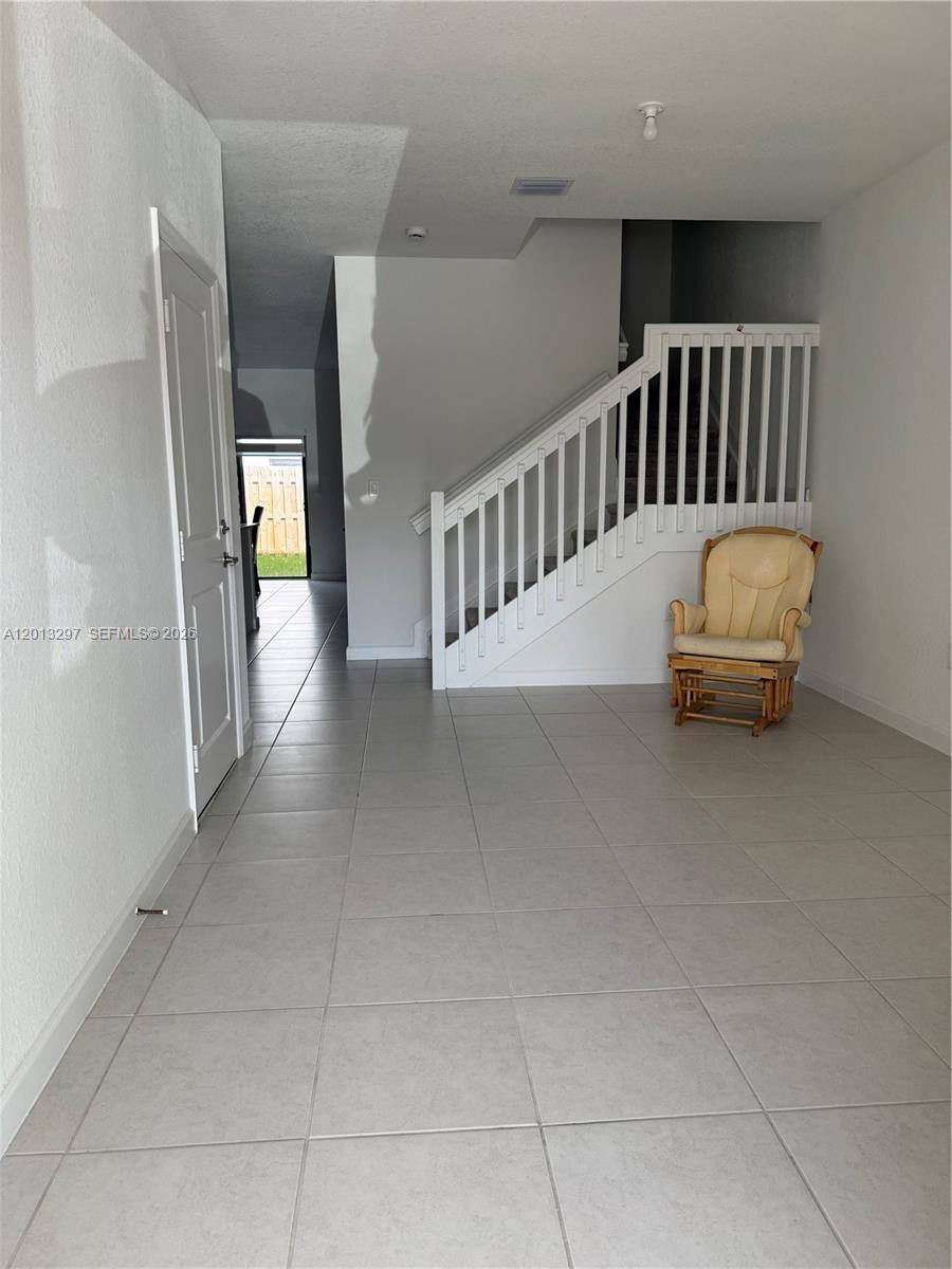 A room with light tile flooring features a white staircase and a wooden rocking chair — 12955 SW 231st Ter # 12955, Miami FL 33170, MIAMI, FL