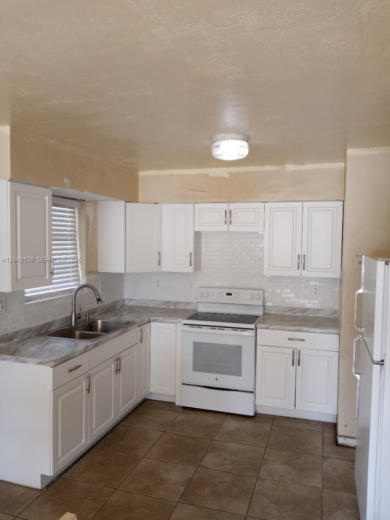 A kitchen features white cabinets, a white stove, a double sink, and tiled flooring — 2901 NW 50th St, Miami FL 33142, MIAMI, FL