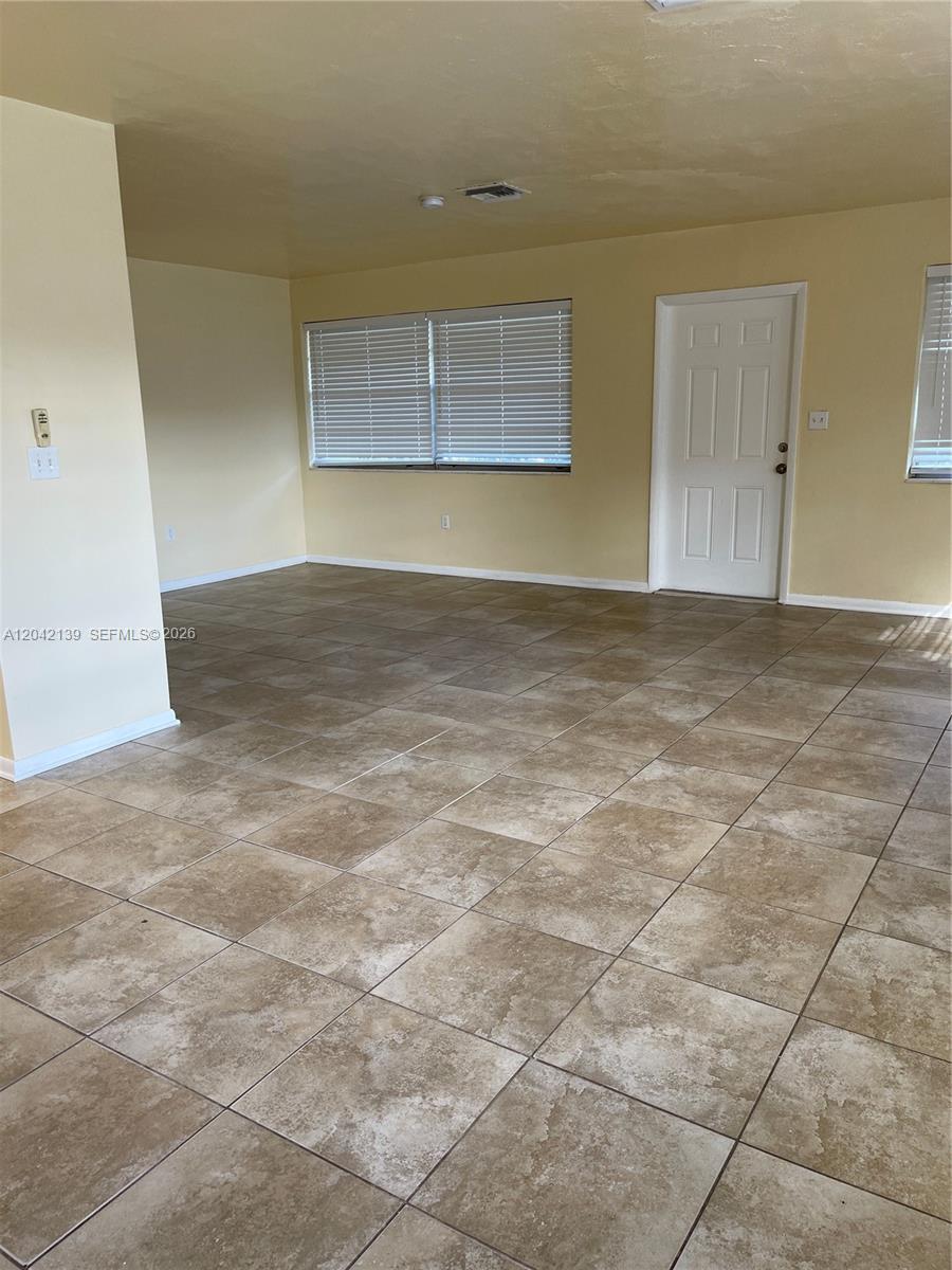 An empty room features light yellow walls, large square floor tiles, and a white door — 2901 NW 50th St, Miami FL 33142, MIAMI, FL