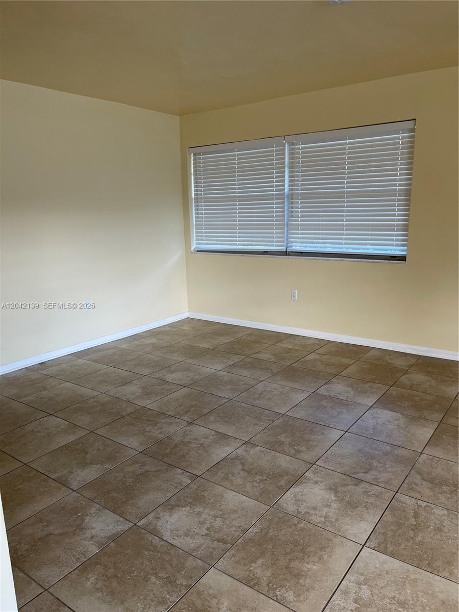 An empty room features light yellow walls, large square floor tiles, and white window blinds — 2901 NW 50th St, Miami FL 33142, MIAMI, FL