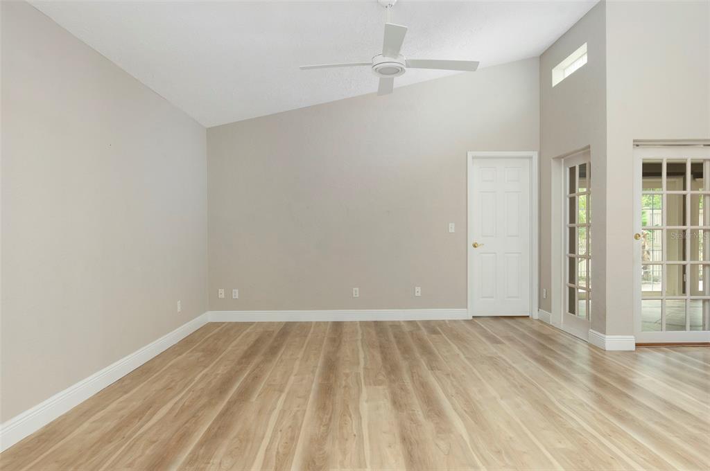 An empty room with light wood-look flooring, beige walls, a ceiling fan, and glass doors — 491 ST TROPEZ CIRCLE NE, ST PETERSBURG, FL