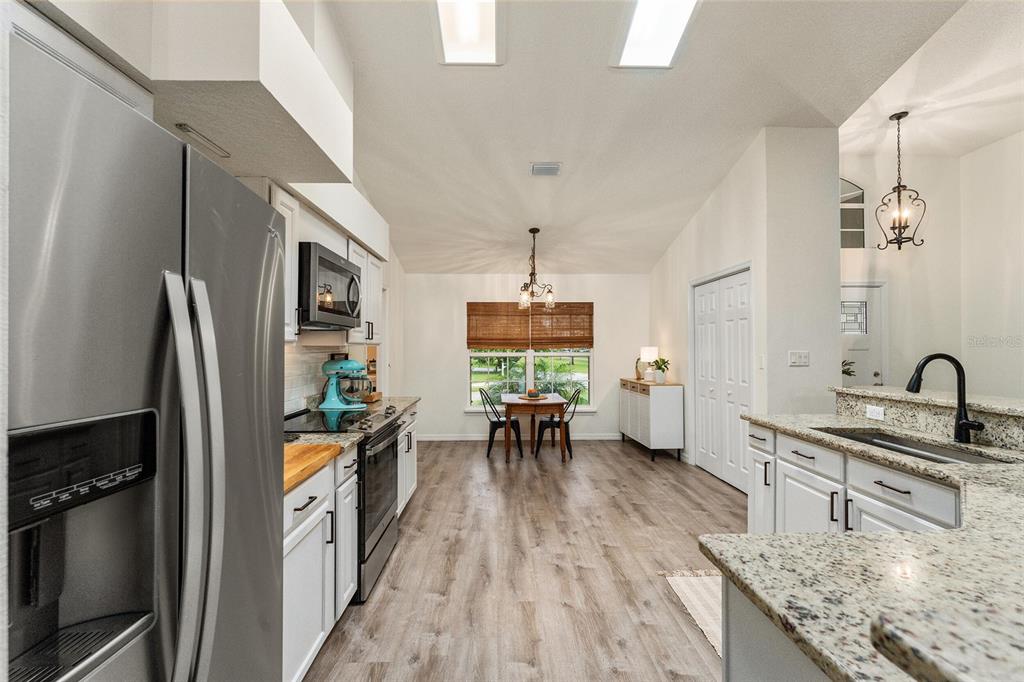 A kitchen with white cabinets, granite countertops, stainless steel appliances, and an adjacent dining area — 7237 EDMUND COURT, MOUNT DORA, FL