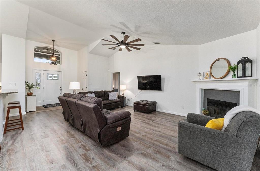 A living room features a vaulted ceiling, wood-look flooring, a fireplace, and brown furniture — 7237 EDMUND COURT, MOUNT DORA, FL