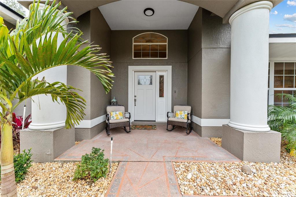 A covered front porch features two rocking chairs, a white door, and large columns — 7237 EDMUND COURT, MOUNT DORA, FL