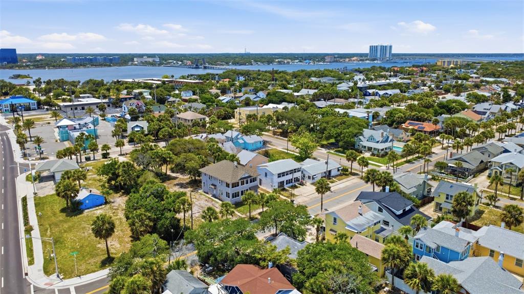 An aerial view shows a coastal neighborhood with houses, palm trees, and a distant bridge — 215 S OLEANDER AVENUE, DAYTONA BEACH, FL