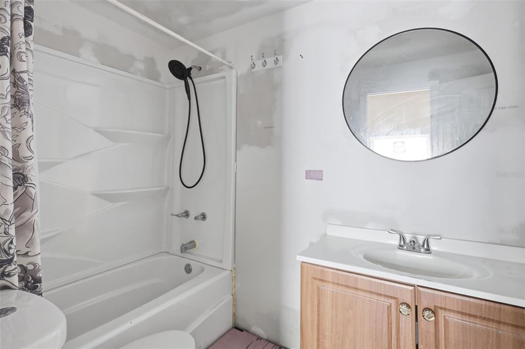 A bathroom features a white tub-shower combo, a wooden vanity, and unfinished drywall walls — 215 S OLEANDER AVENUE, DAYTONA BEACH, FL